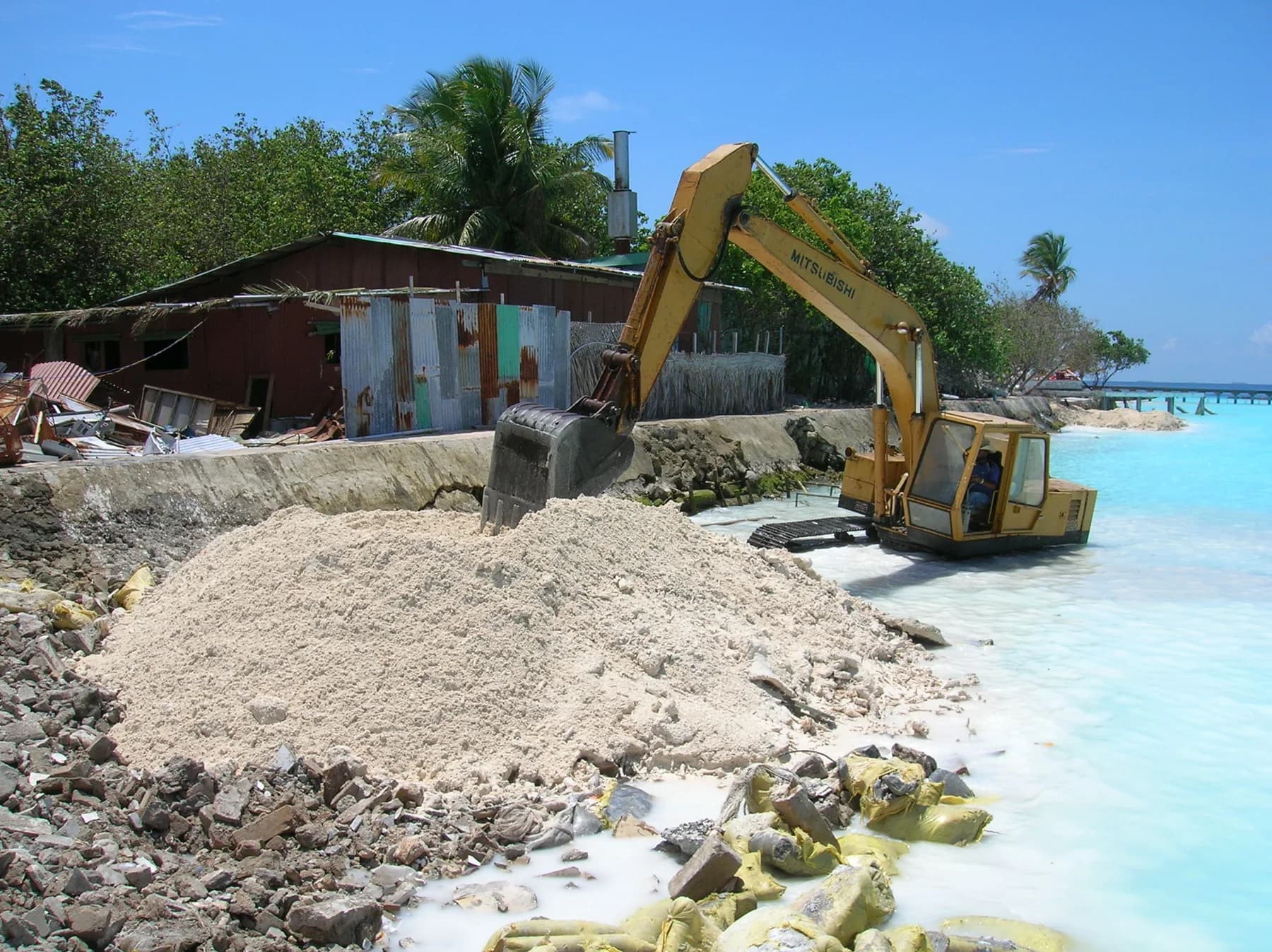 Excavator clearing demolition debris on a resort shoreline