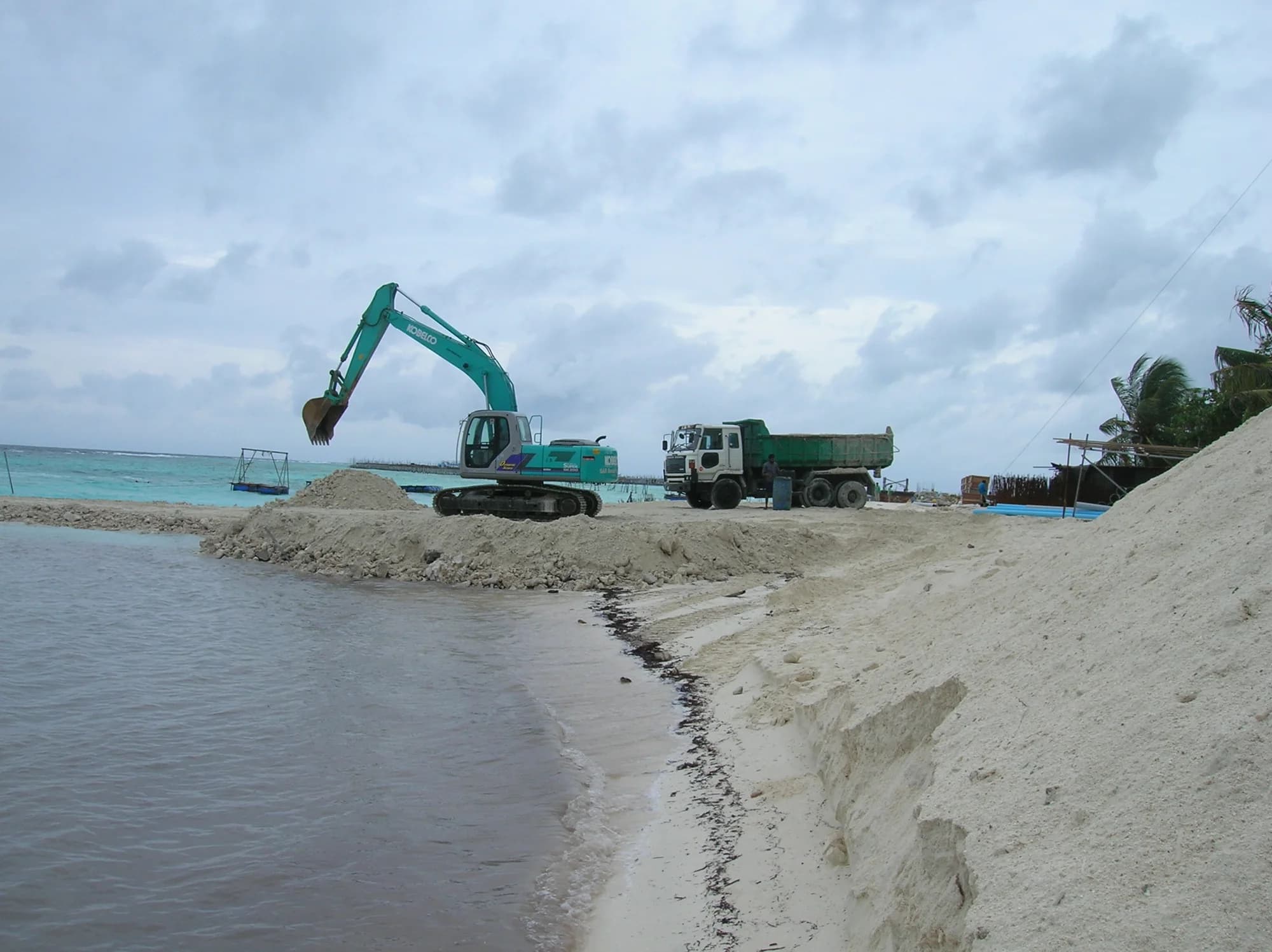 Excavator and dump truck working a dredged channel in shallow turquoise water
