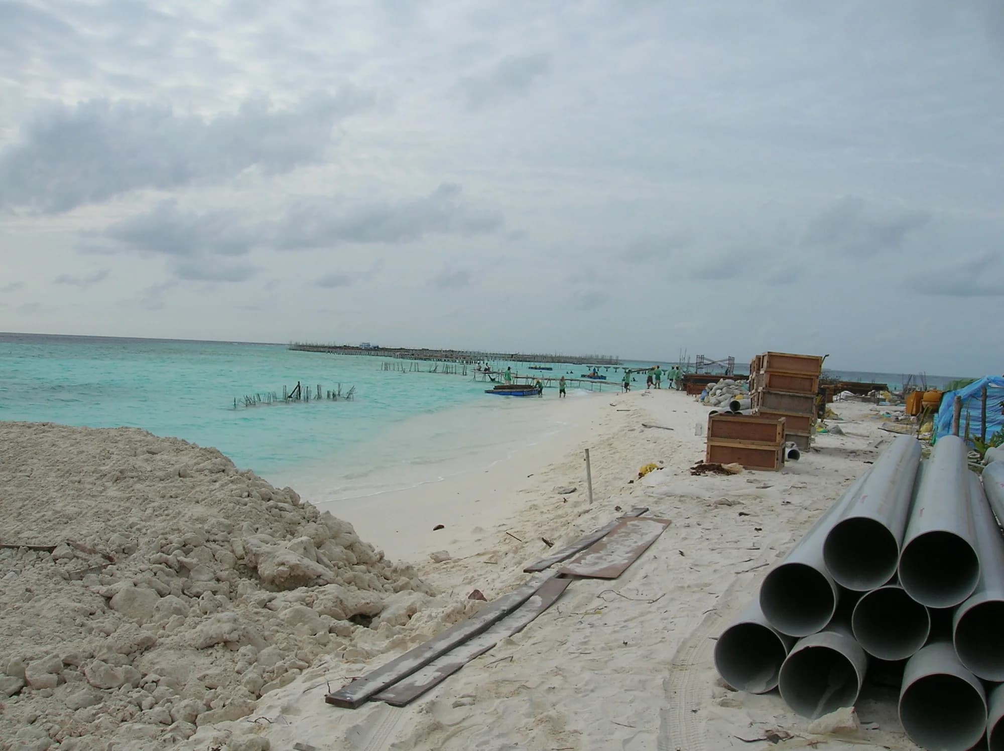 Stacked pipe on the beach and workers assembling a staked pipe run across the shallows