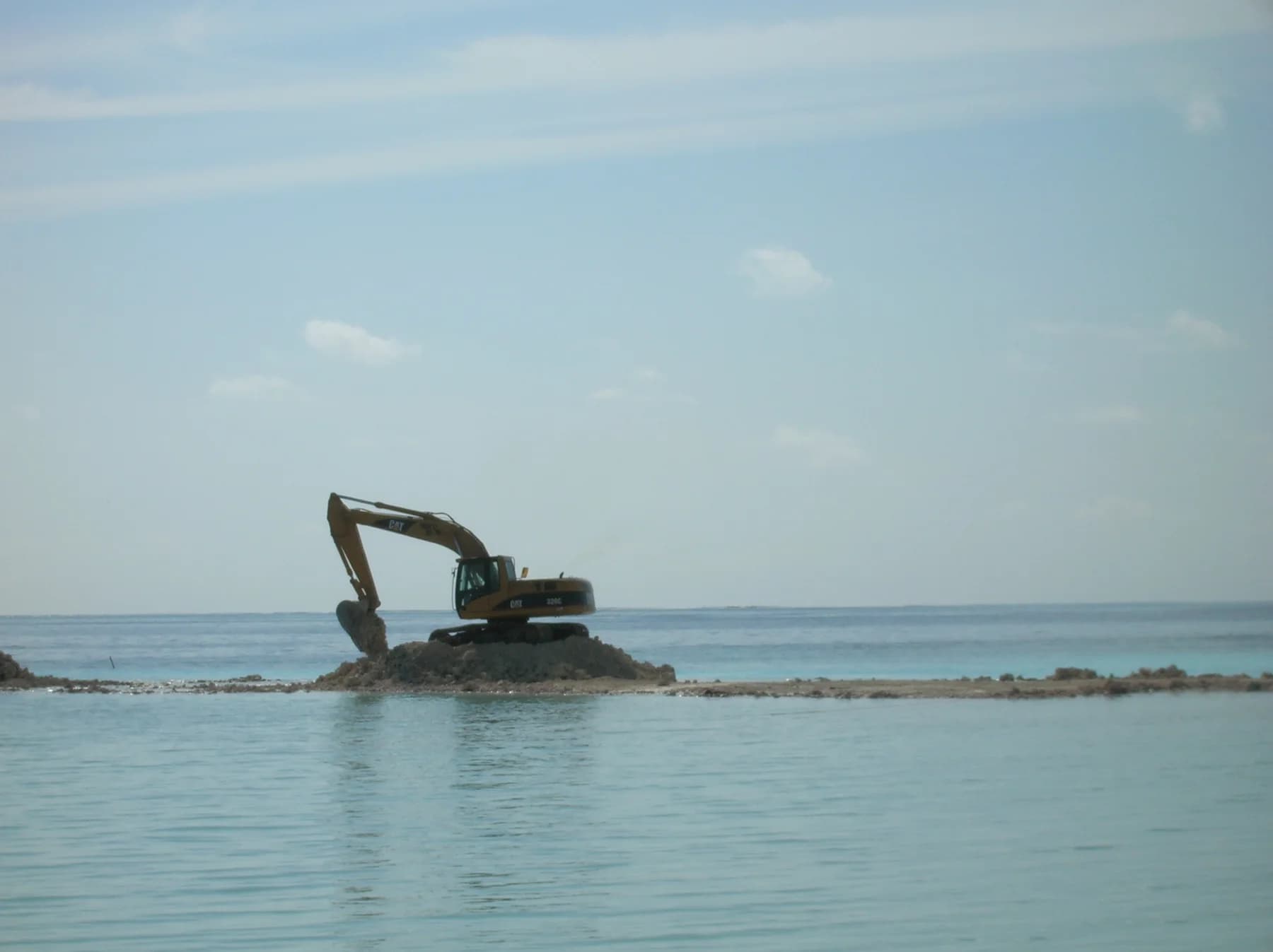 A long-reach excavator dredging from a sandbar out in the lagoon
