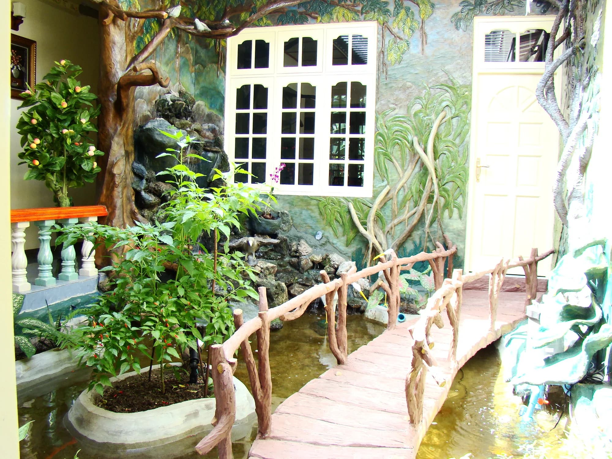 Internal water garden with a cast-concrete footbridge over a pond, moulded rockery and painted jungle mural