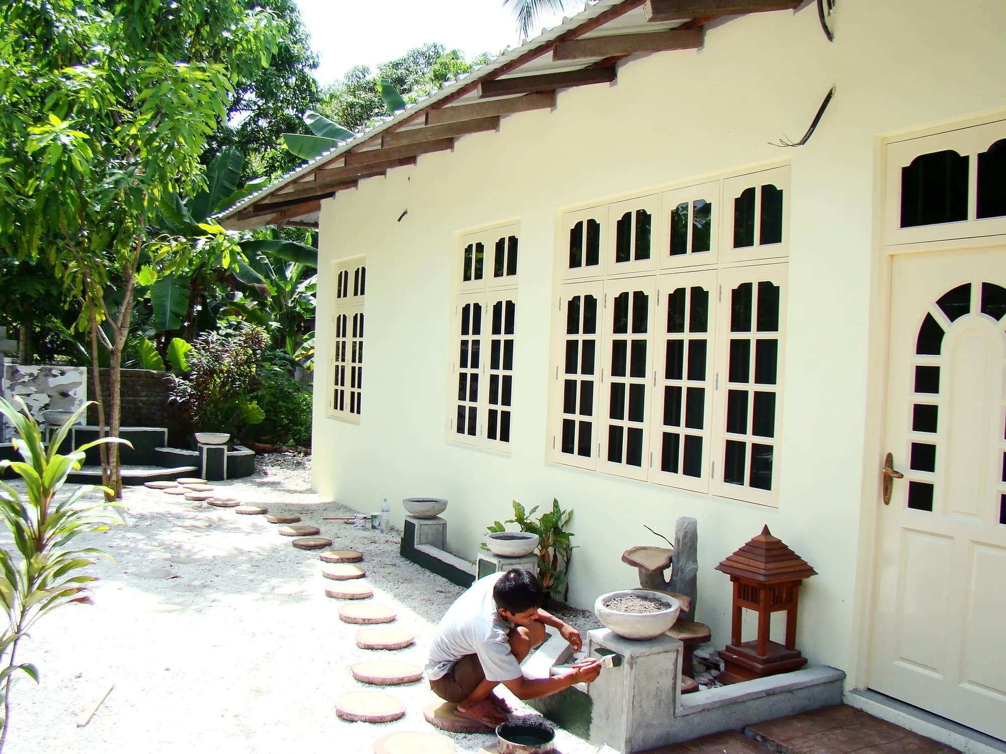 White rendered single-storey house with arched multi-pane casement windows, a worker finishing a garden plinth