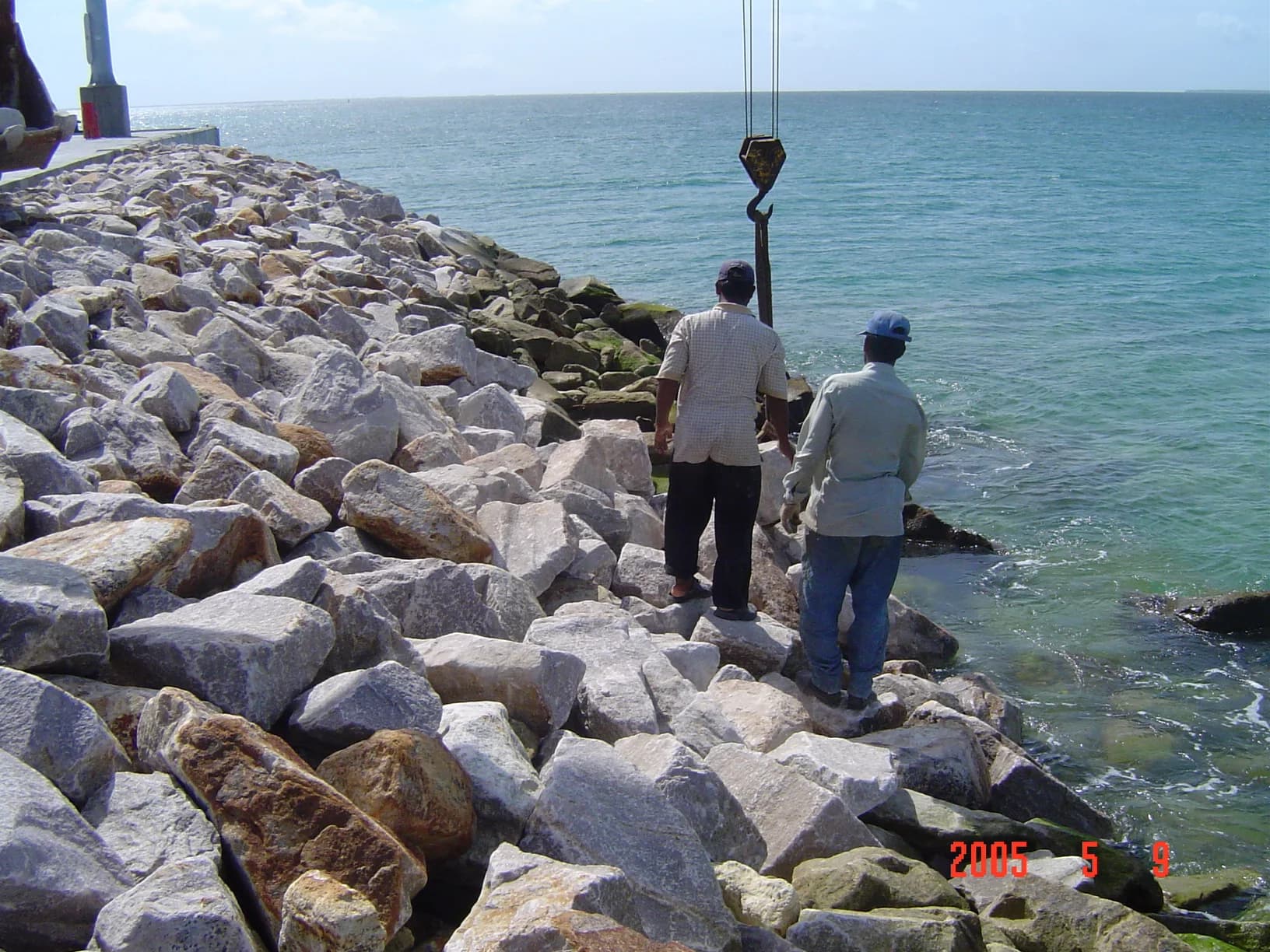 Workers on the armour-rock slope of a breakwater as a crane places stone