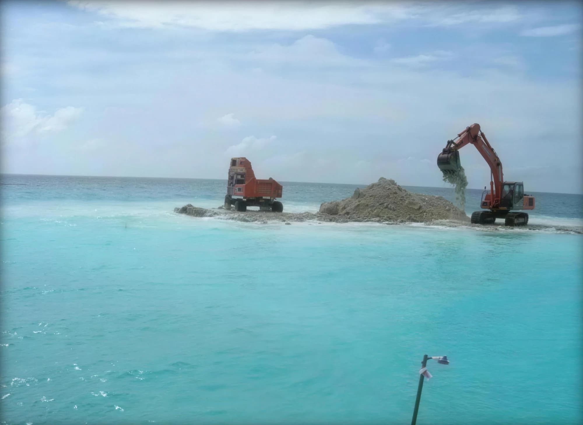 Excavator dredging a harbour channel in shallow turquoise water